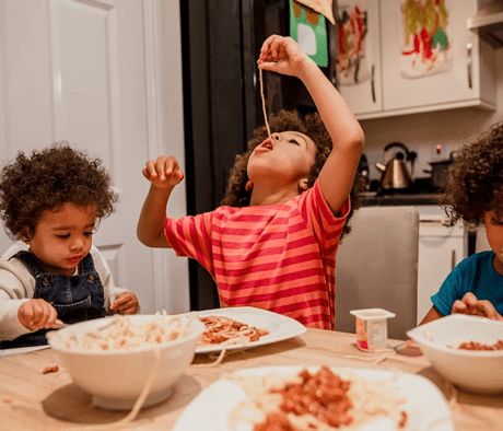 Three children eating good food at a table