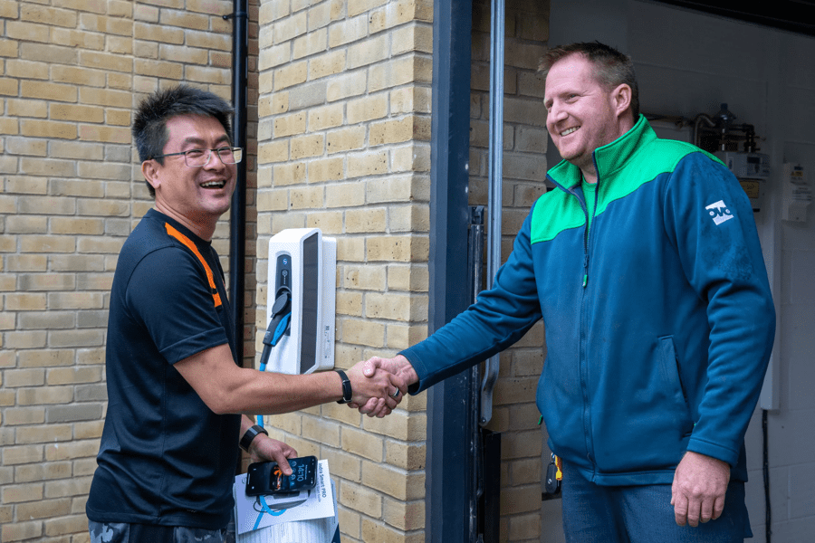 OVO engineer shakes hands with customer. The EV charger is installed behind them.