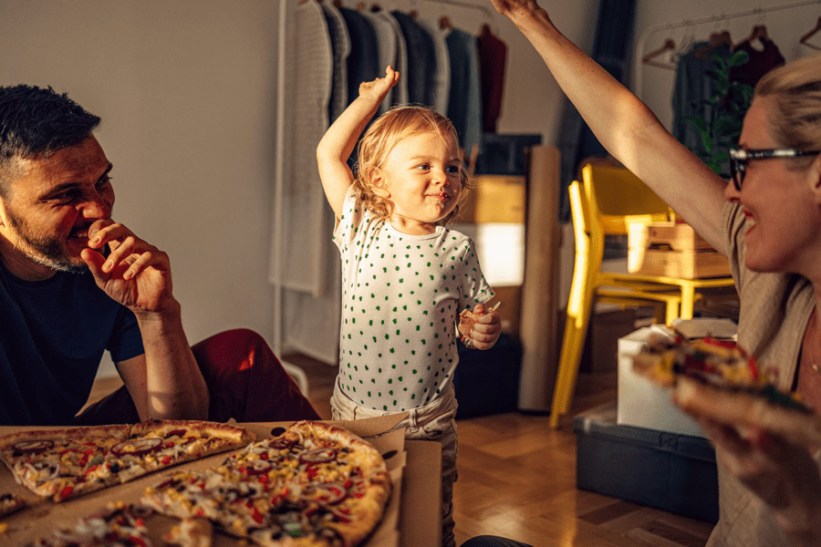 a young girl playing with her parents as they eat a pizza