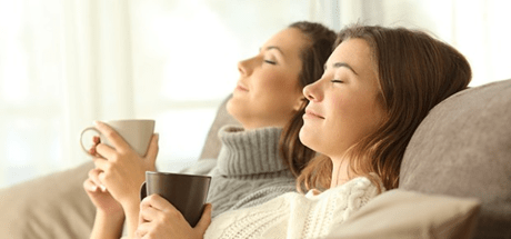 Two women sitting on a sofa holding mugs