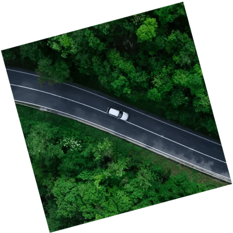 An aerial view of a car driving along road in the green countryside