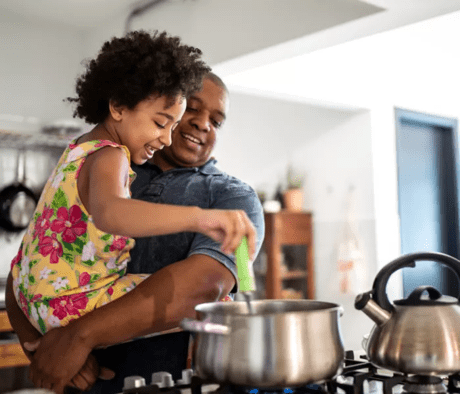 A father and daughter cooking a dish in a saucepan in their kitchen