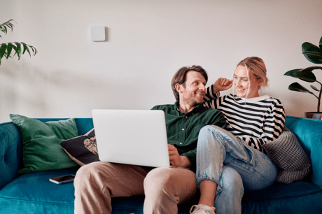 A man and a woman sitting on a blue couch. The man has a laptop on his lap.