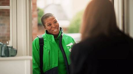 OVO engineer in a green jacket smiling while speaking to a customer at the door.