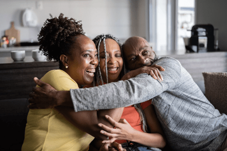 Three smiling people sitting down and hugging