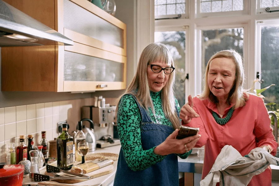 two women standing in a kitchen, looking at a phone