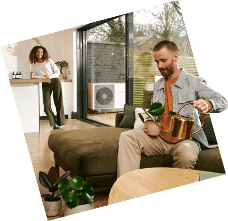 Young couple in kitchen. The man is watering his plants while the woman leans against the counter.