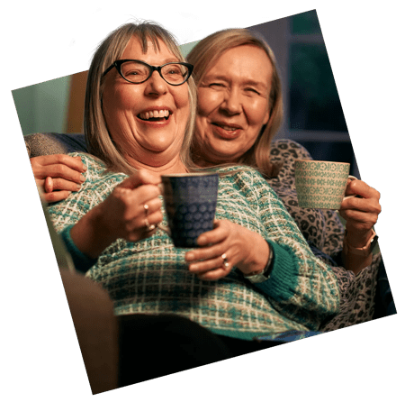 Two women holding mugs and laughing 
