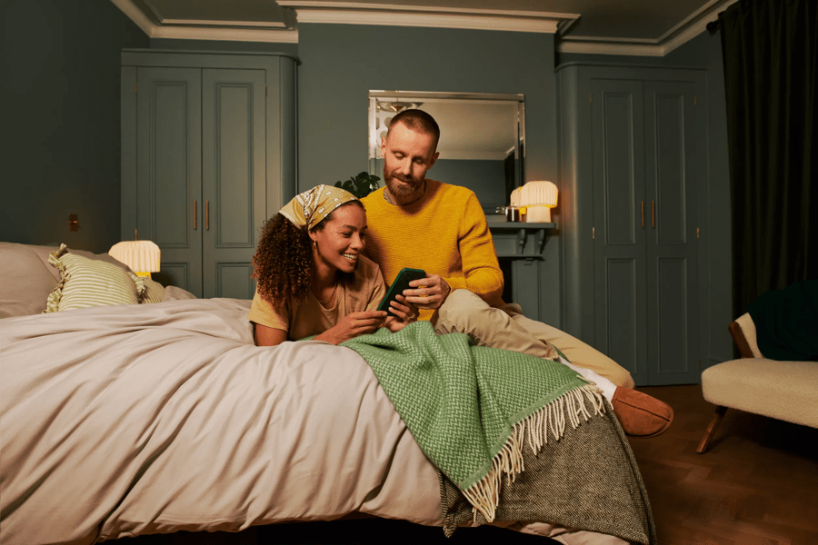 man and woman sitting on a bed looking at a phone