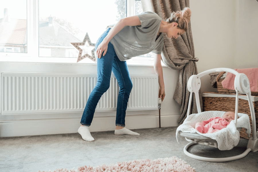 A woman adjusts the radiator temperature next to her baby