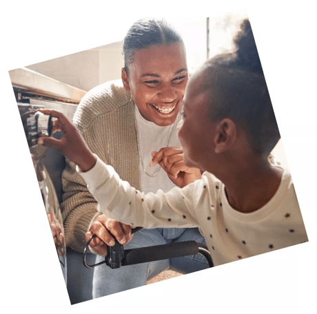 Mother and daughter laughing as they use the washing machine