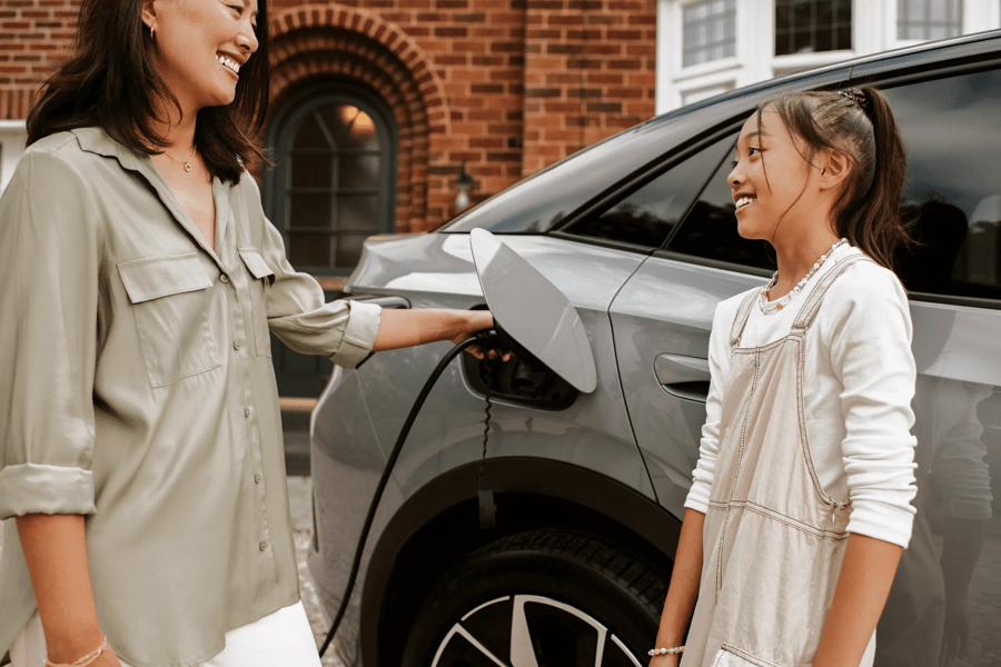 woman charging an electric car with her daughter nearby 