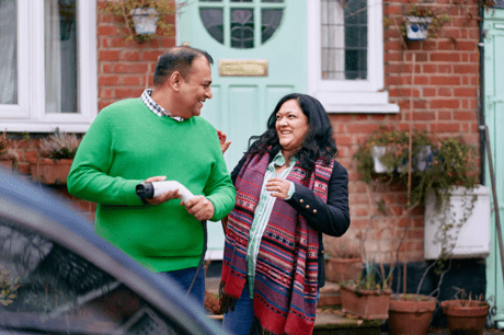 A man holding an EV charger outside a house, chatting to a woman