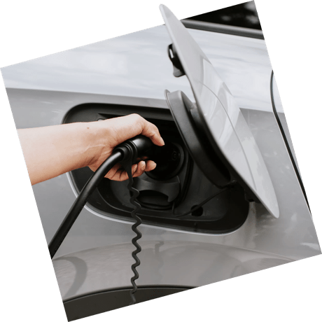 A hand plugs an EV charger into the port of a silver electric vehicle.