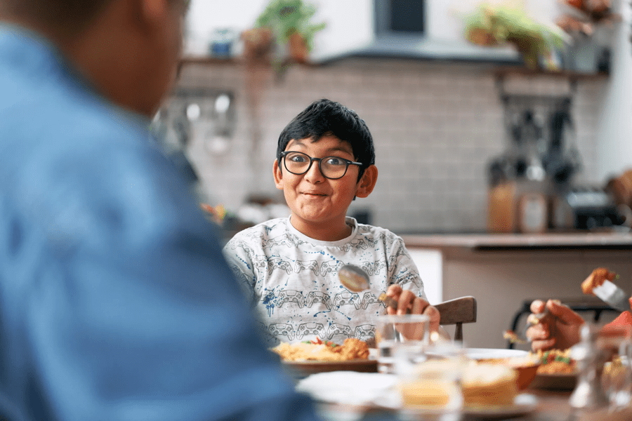 a young boy with glasses sitting at a table eating breakfast