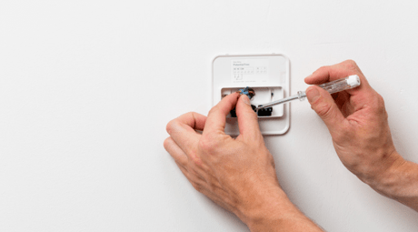 A customer fitting their own tadoº smart thermostat onto a wall using a small screwdriver